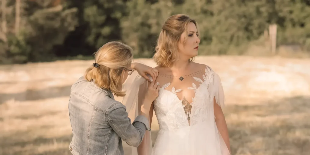 Irina richtet einer Braut das Kleid, im Hintergrund ein sommerliches Feld